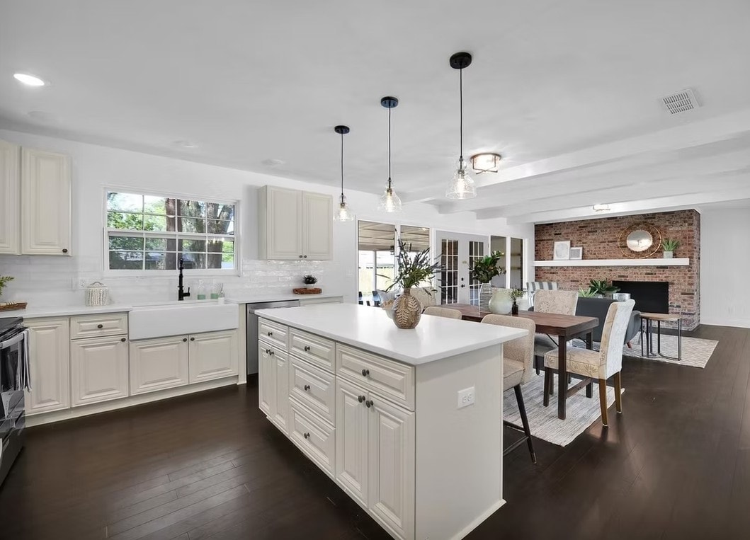 Open Pearl White kitchen with center island, pendant lights and brick fireplace