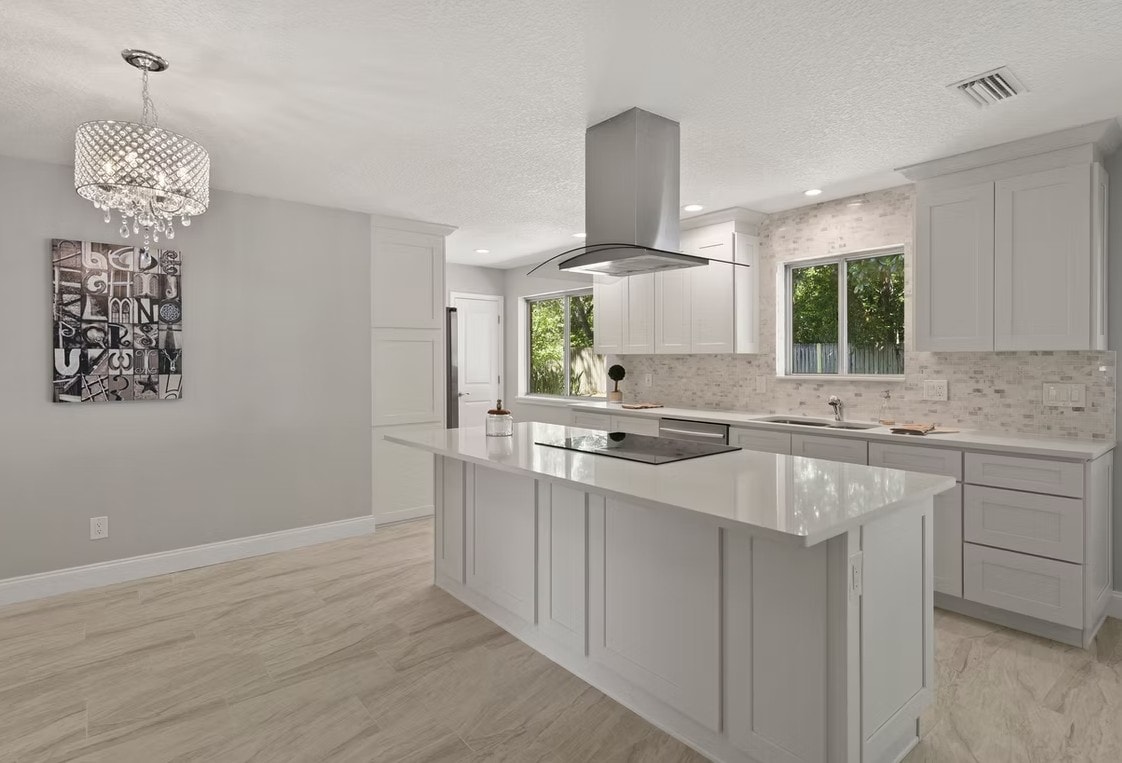 White Shaker kitchen with large island, stainless hood, mosaic backsplash and crystal pendant light