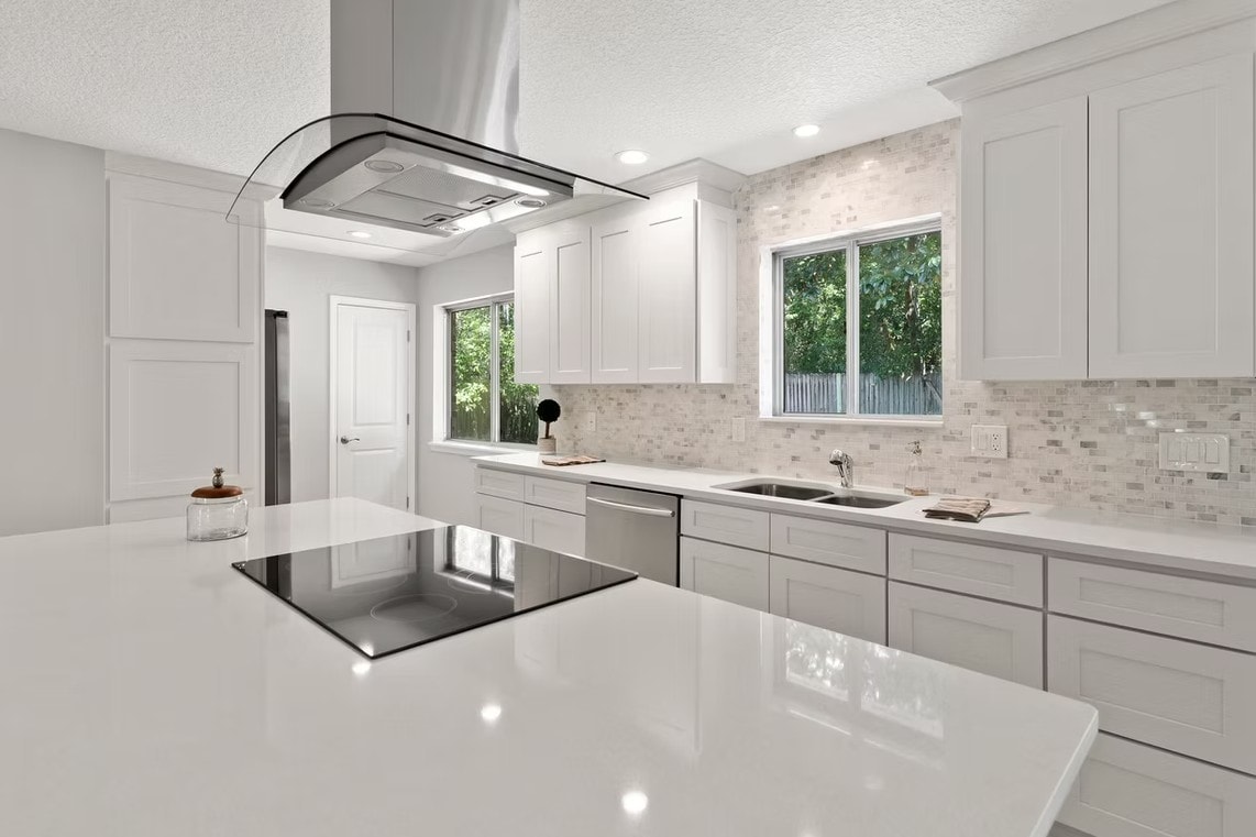 Detail of White Shaker island with bright white countertop and curved stainless hood