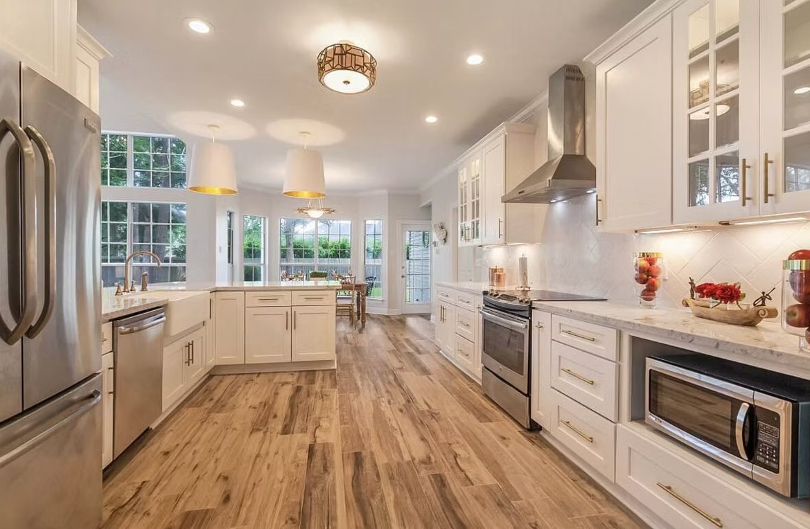 Spacious White Shaker kitchen with island, gold pendant lights, hardwood floor and stainless appliances