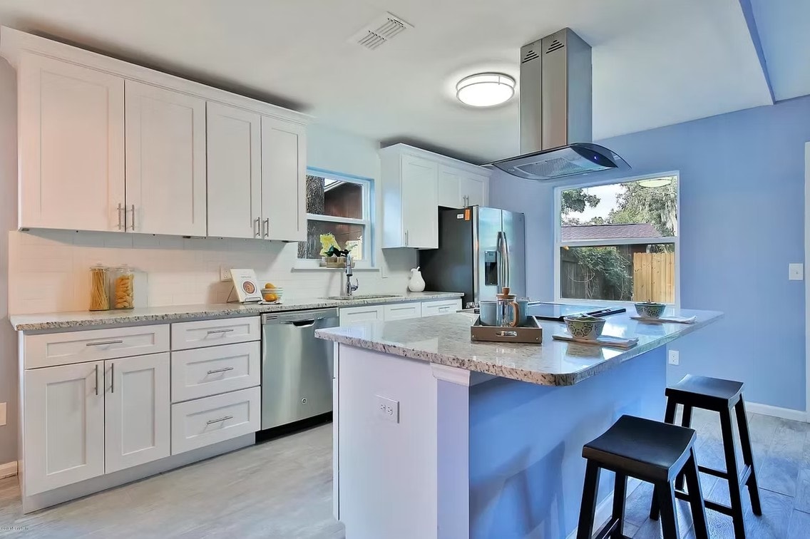 White Shaker kitchen with island, black stools, stainless hood and blue walls