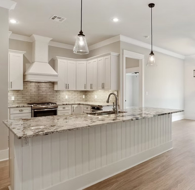 White Shaker kitchen with long island, white granite countertop, white hood and pendant lights
